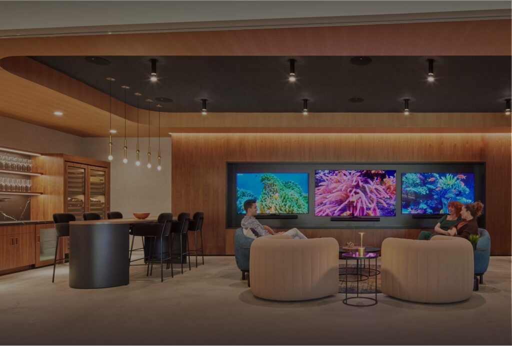 Lounge and bar area at Poms & Associates in Calabasas, built by GCX, featuring walnut millwork, a marble-backed bar with wine storage, curved seating, and a three-screen media wall.